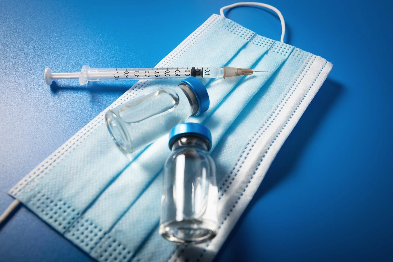 A vaccine vial and syringe on a clinic table, shown close-up in soft daylight.