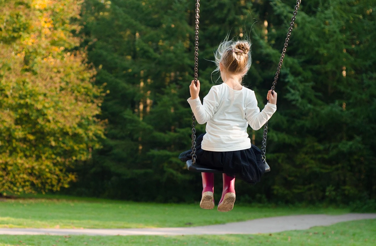 A fenced-off children's playground in an Ontario park in autumn, surrounded by trees with orange and fallen leaves.