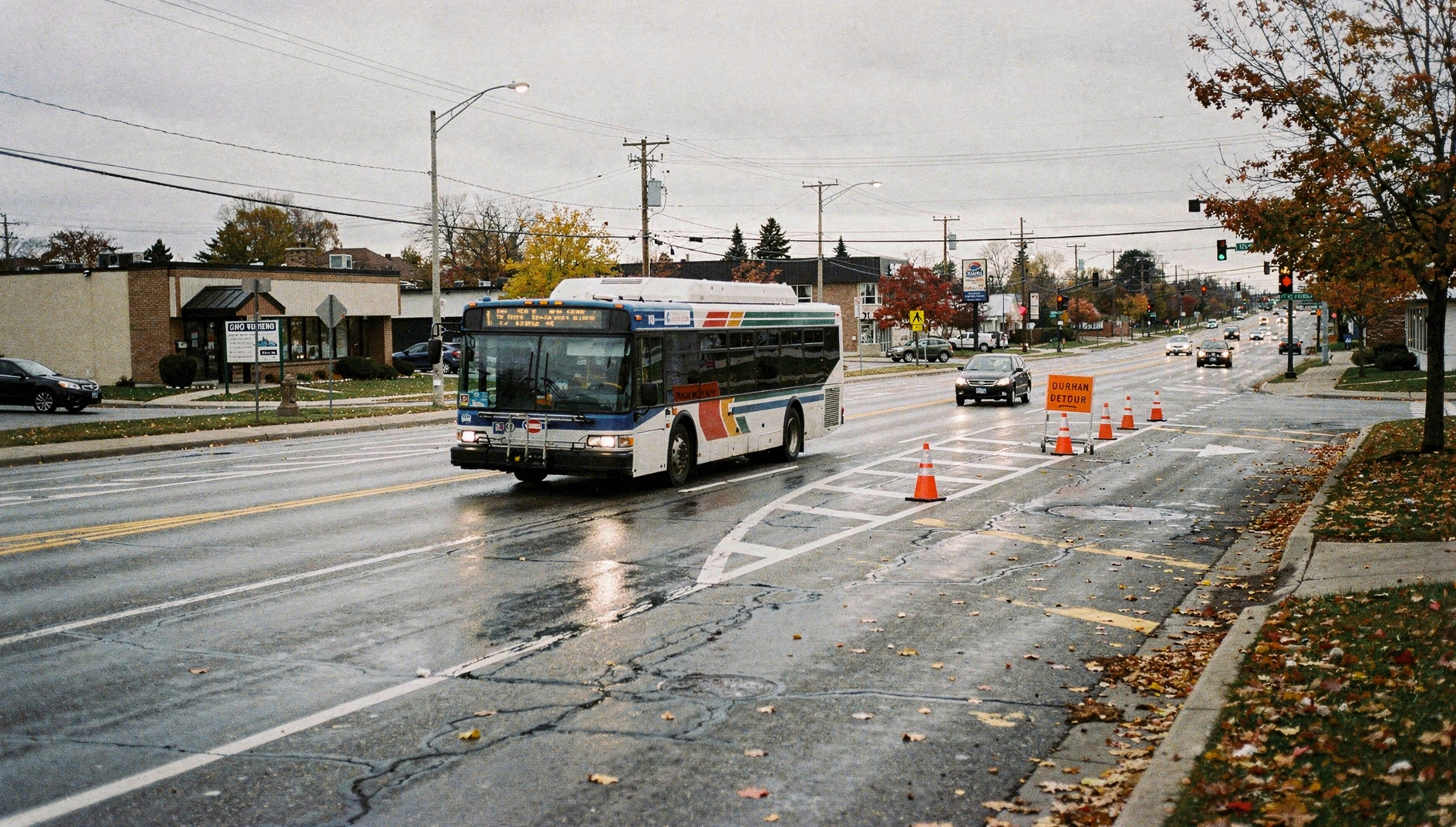 A city bus passes road construction detour signs on a suburban arterial road in autumn.