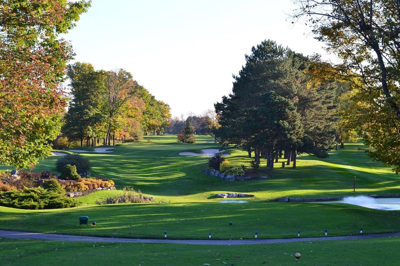 A view of a lush green golf course fairway with a sand trap under an autumn sky.