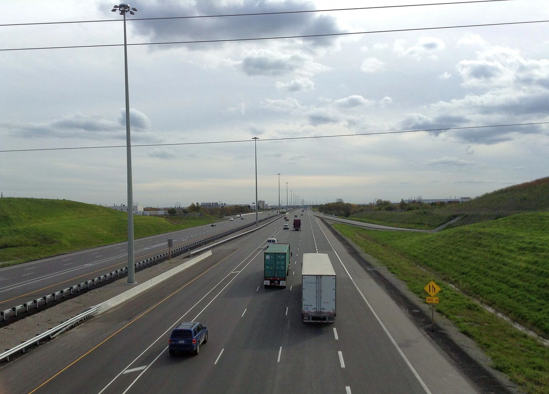 Commuter traffic moving along a multi-lane highway ramp under a grey October sky near a large interchange.