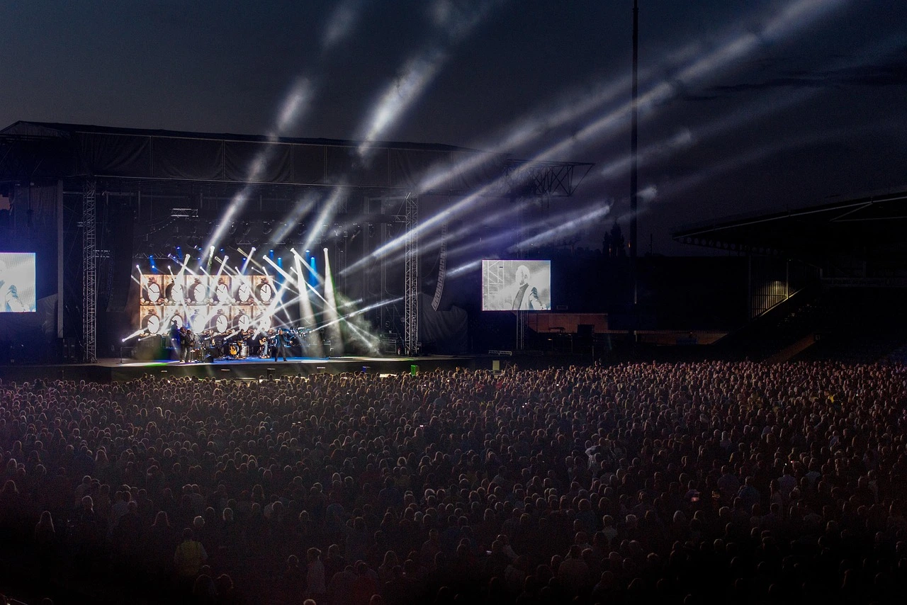 An outdoor concert stage with bright lights set up at night near the mist of a large waterfall.