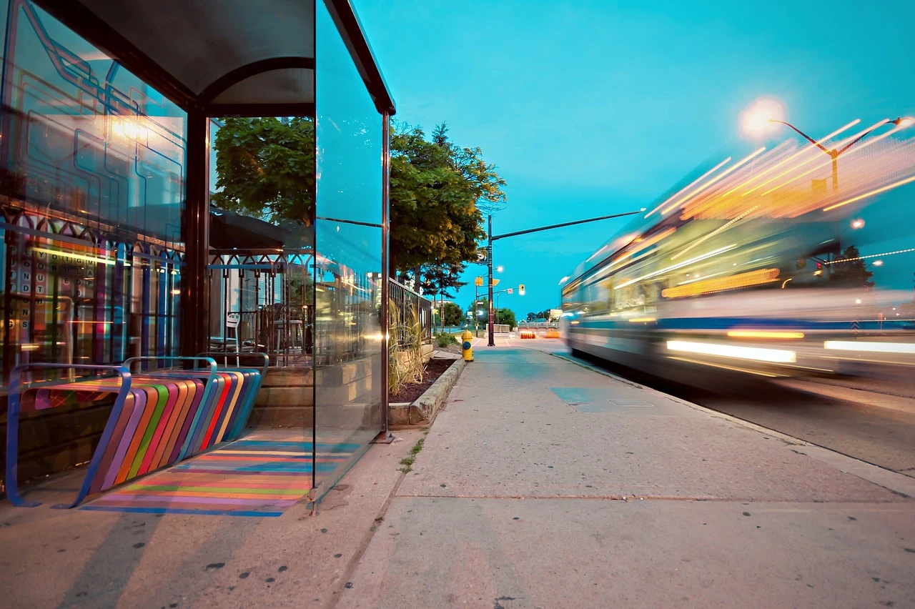 A city bus stops at a shelter on a tree-lined suburban street in autumn.