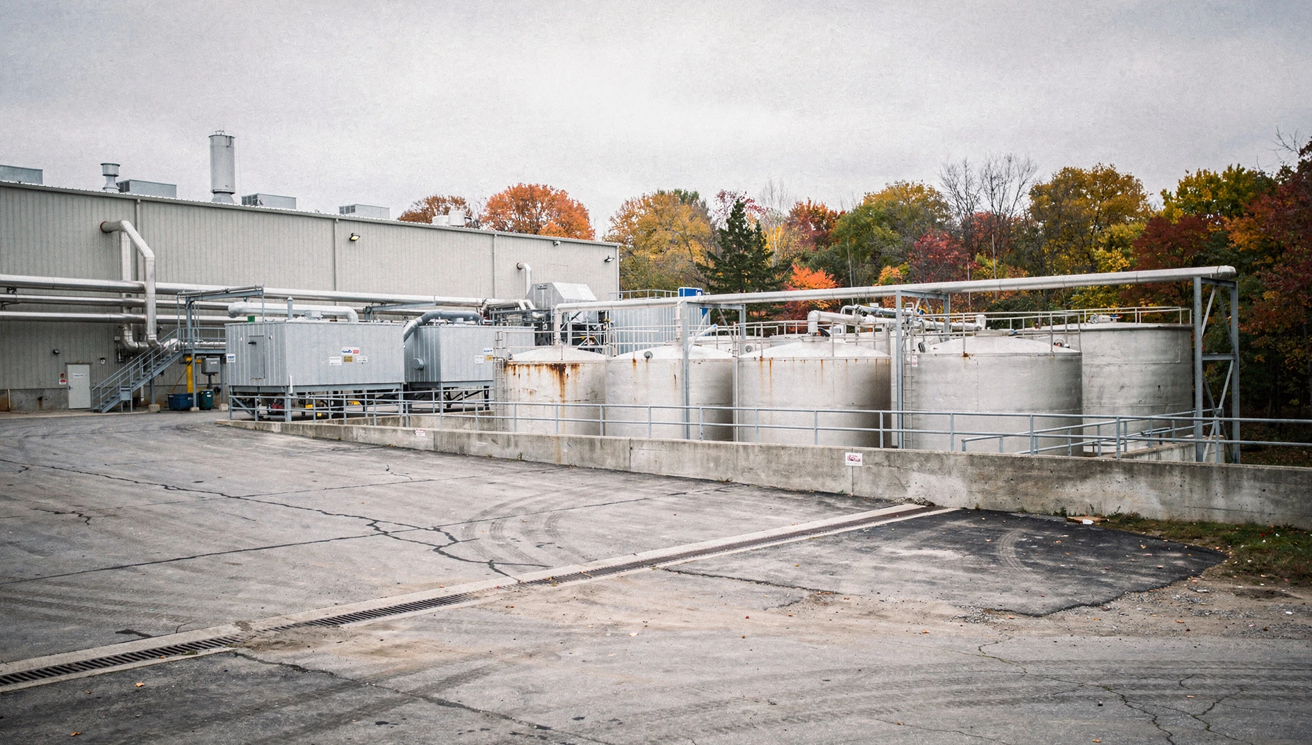 Industrial organics processing buildings and digestion tanks beside a service yard, with autumn trees in the background.