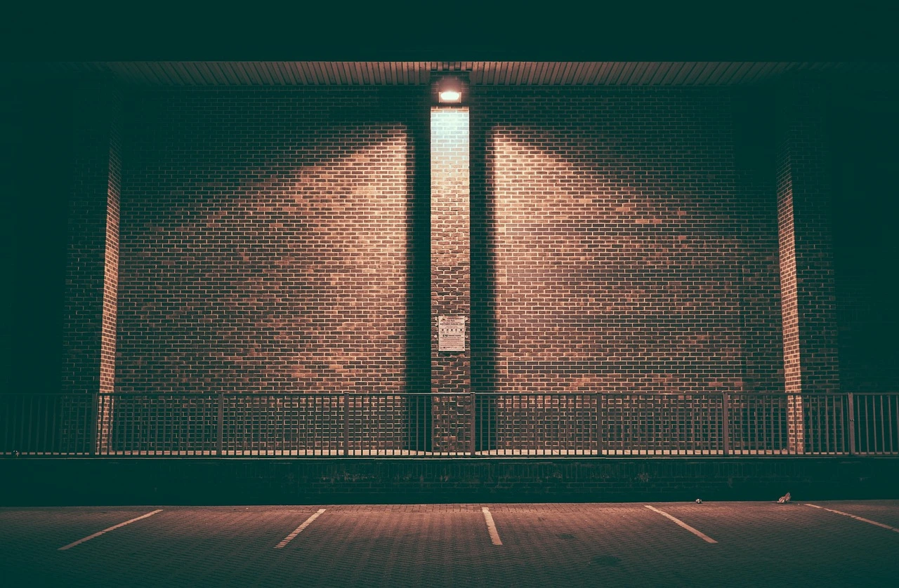 A close-up of yellow police tape stretched across a parking lot at dusk, with blurred red and blue emergency lights in the background.