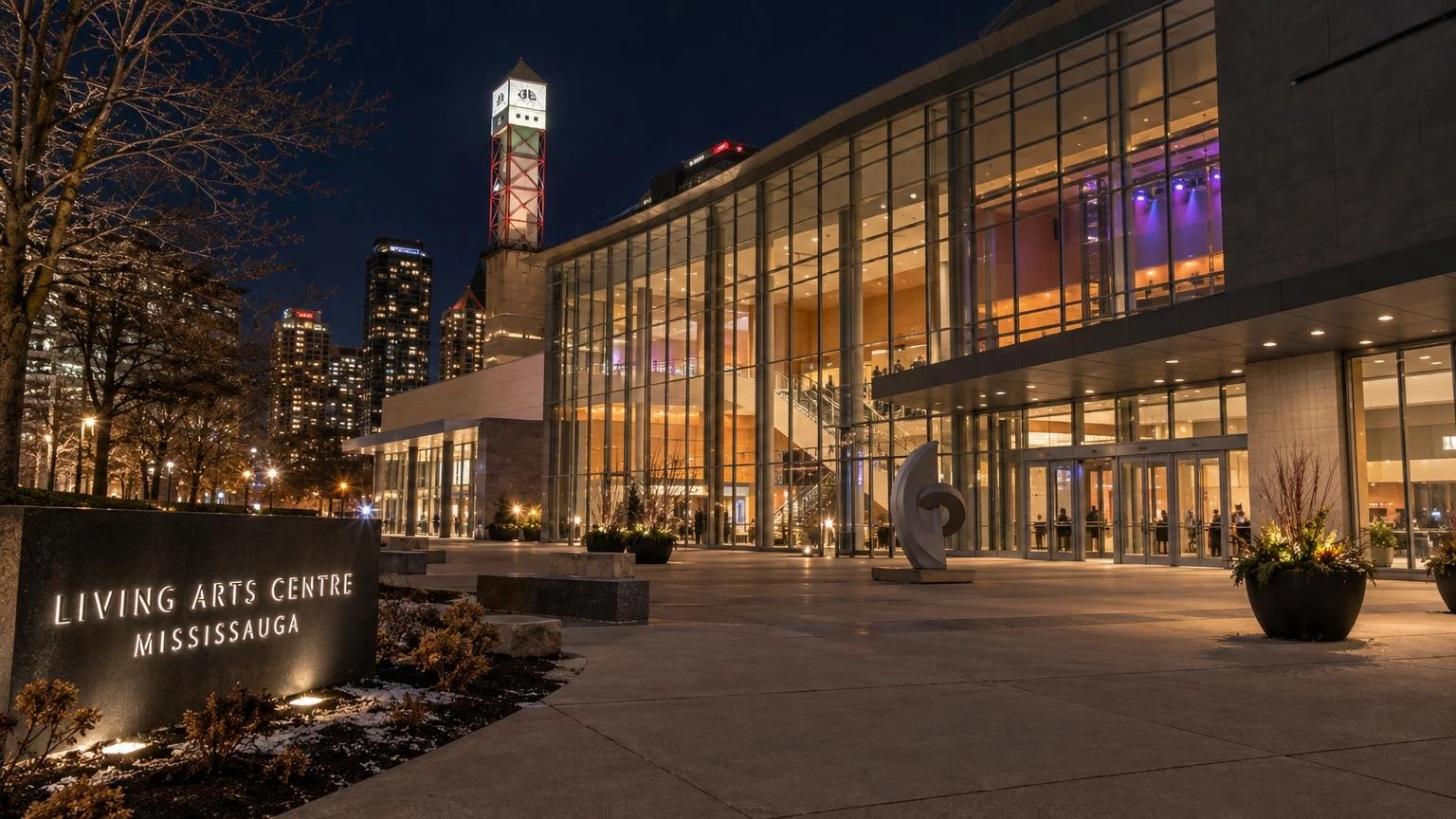 An evening view of the Living Arts Centre in Mississauga with stage lights glowing through the windows.