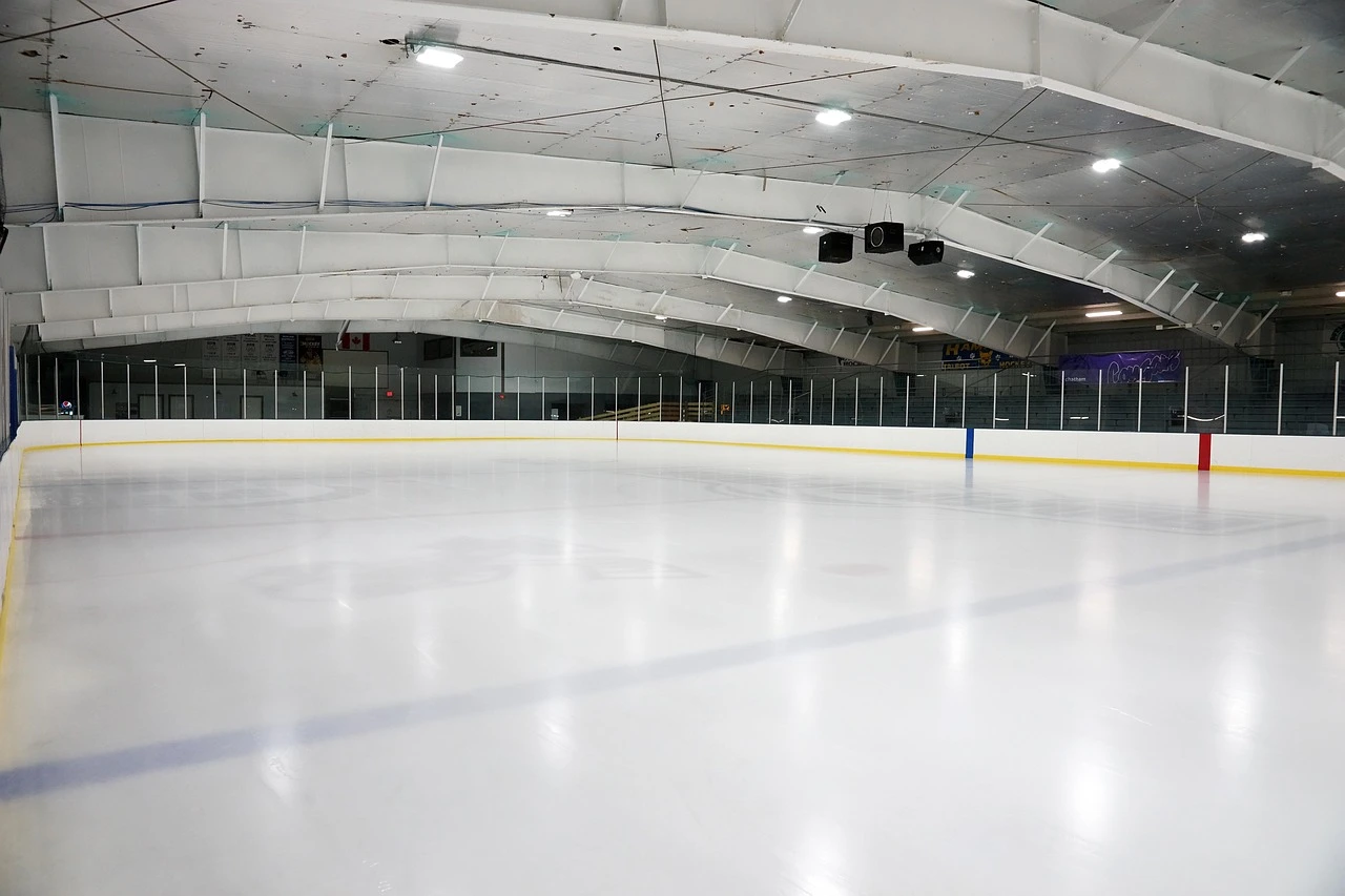 An empty indoor ice rink with bright arena lights and a freshly resurfaced ice sheet.
