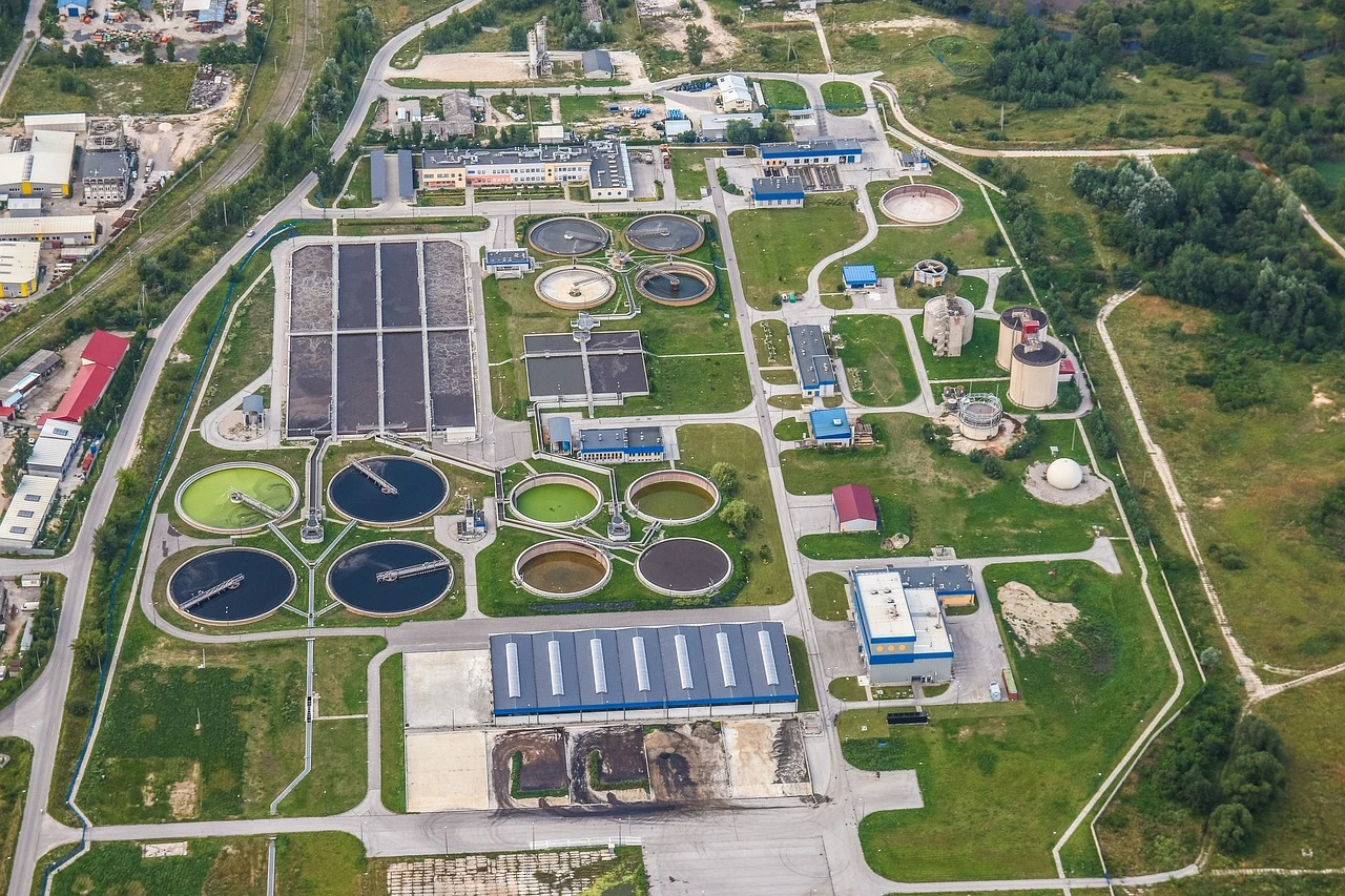 An industrial wastewater treatment facility with large concrete tanks and metal pipes under autumn trees.