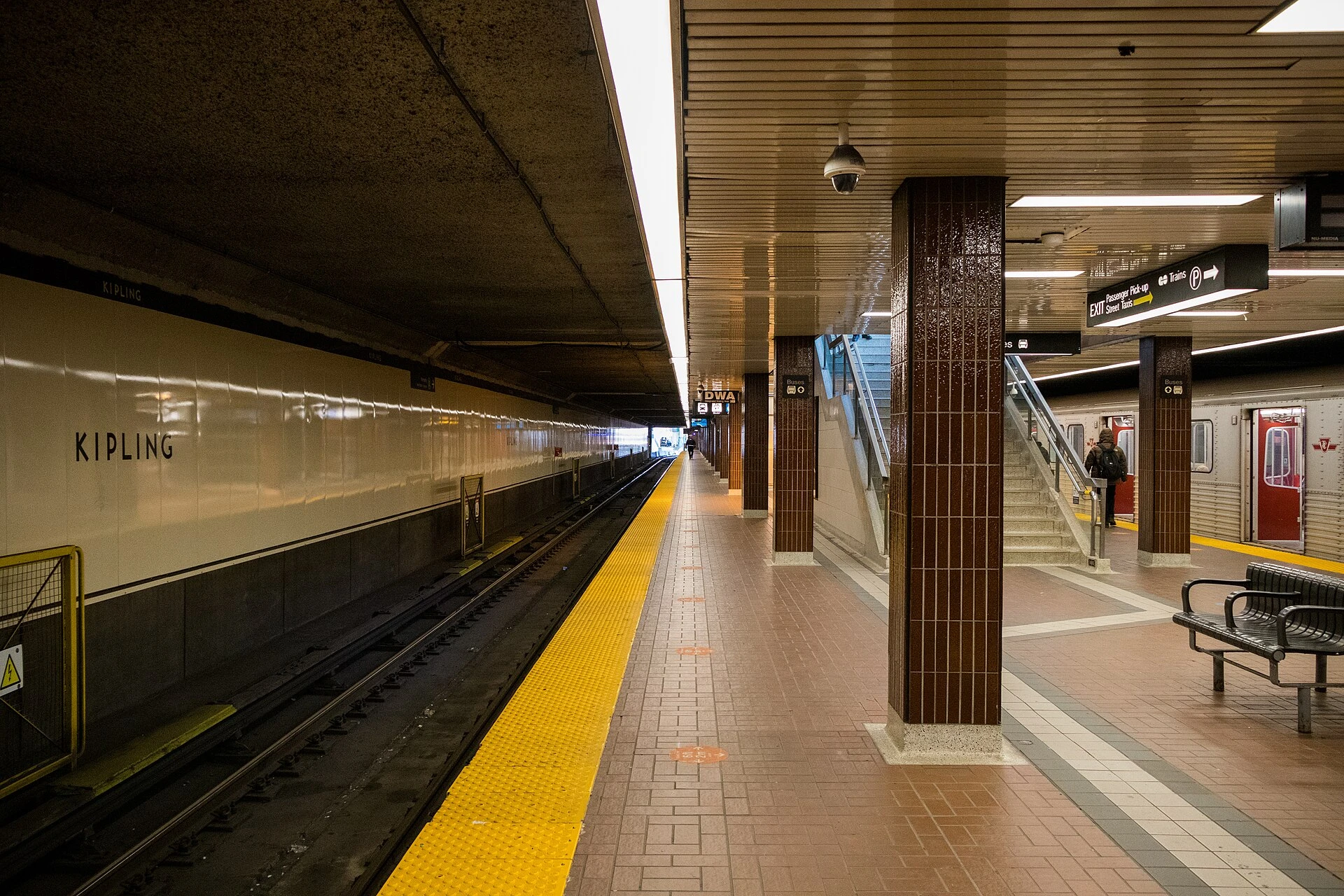 A Toronto subway station entrance at dusk with a replacement shuttle bus at the curb and autumn trees nearby.