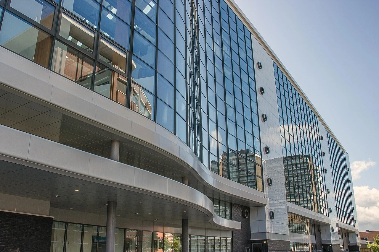 An architectural rendering or conceptual view of a modern hospital building with glass facades under a bright summer sky.