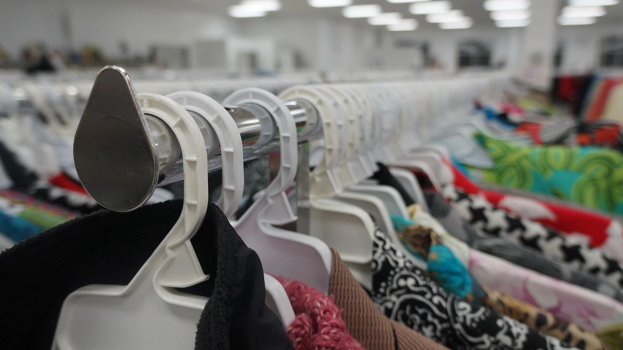 A close-up of a person's hands sorting through various colourful second-hand clothing at a local thrift store.