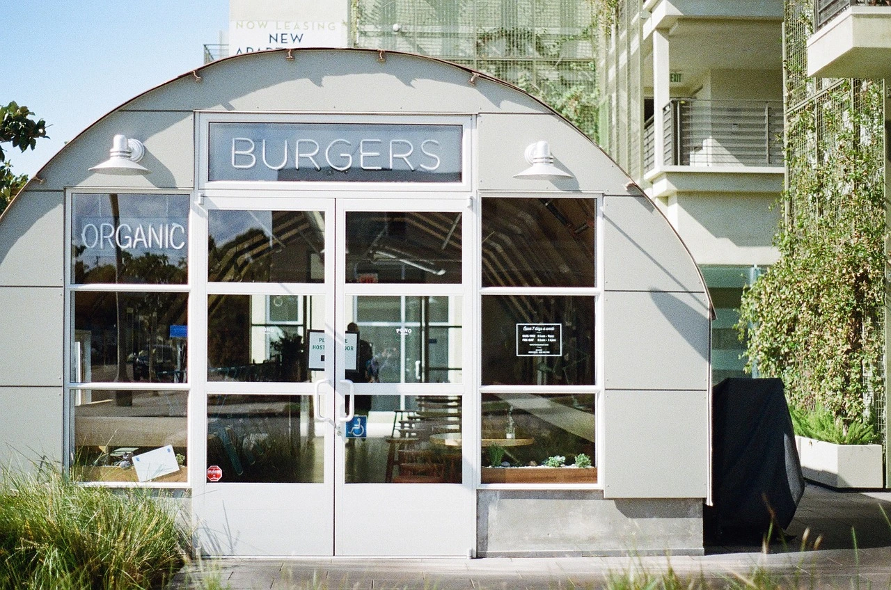 An outdoor view of a modern burger restaurant storefront with outdoor seating in a Mississauga commercial plaza during a sunny summer day.