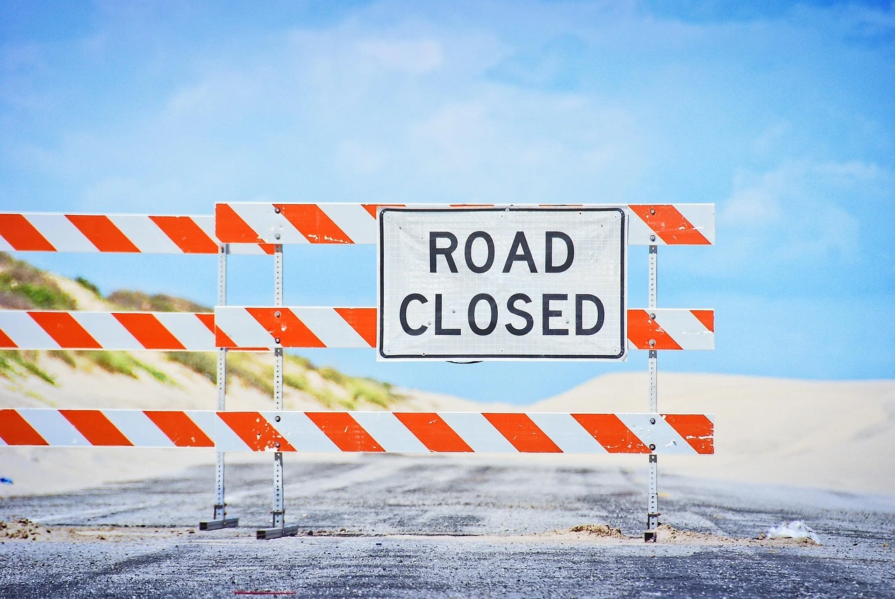 An Ontario intersection closed for roadwork, with orange detour signs and a car stopped near autumn trees.