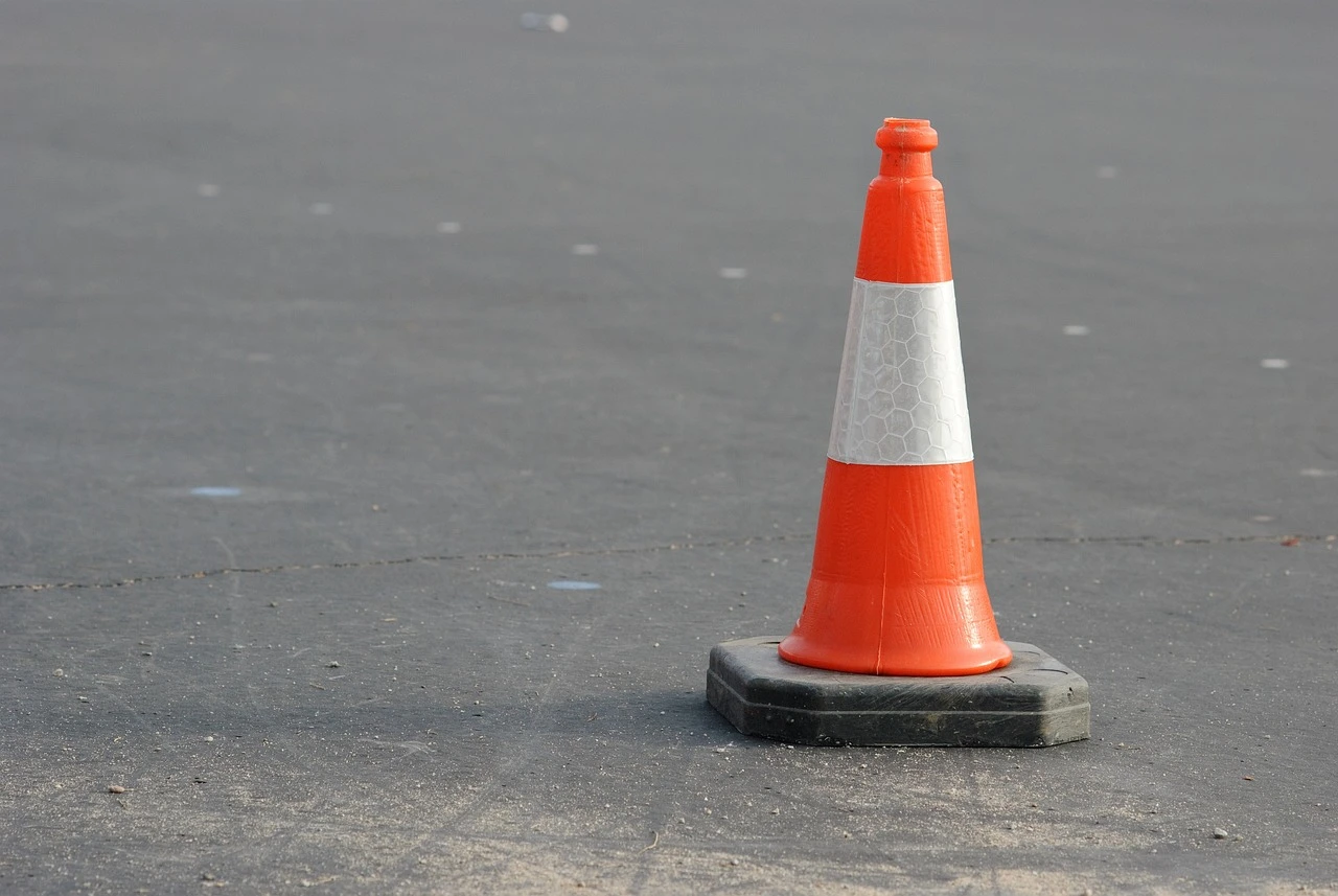 Orange traffic cones narrowing a two-lane suburban road to one lane under an autumn sky.