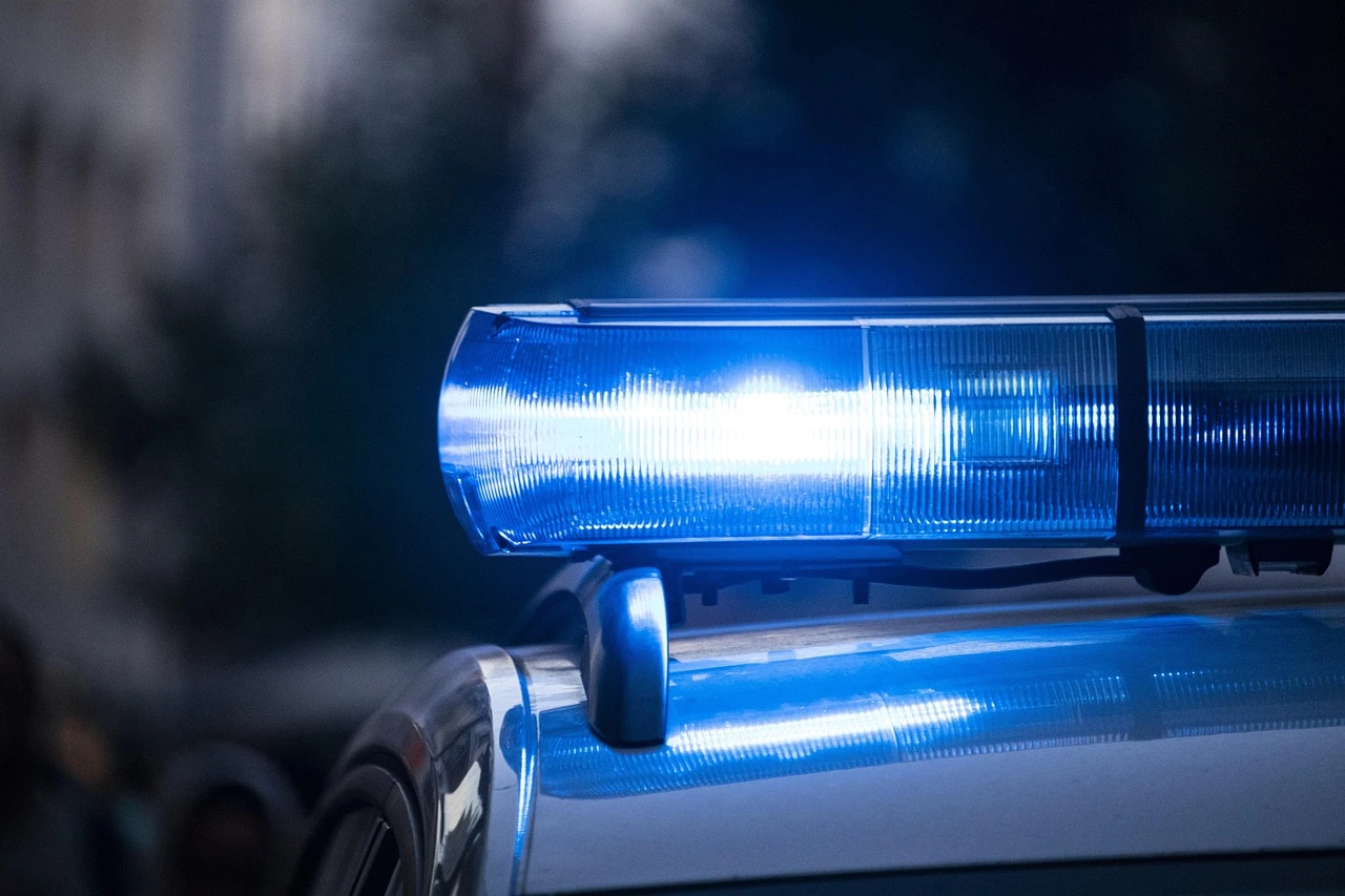 A close-up view of yellow police tape stretched across a roadway at dawn, with blurred emergency vehicle lights in the background.