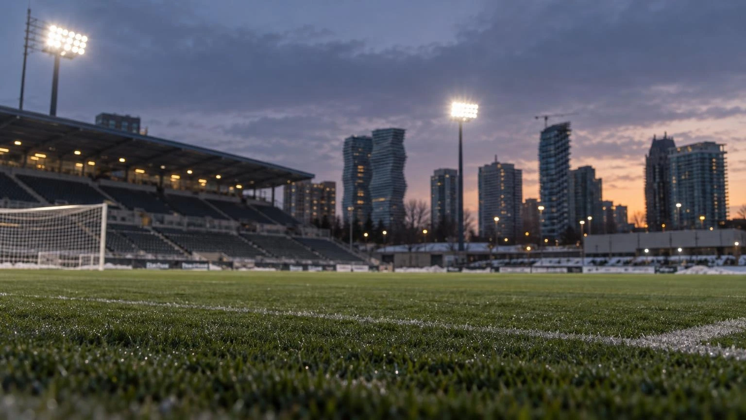 An empty professional soccer pitch under bright stadium lights at dusk.