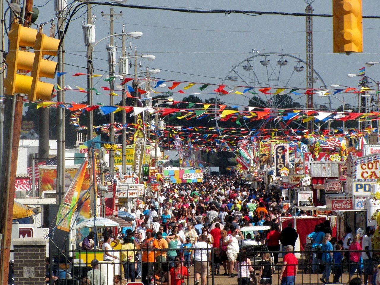 Crowds fill a closed-off city street lined with food vendors and restaurant patios during a summer street festival.
