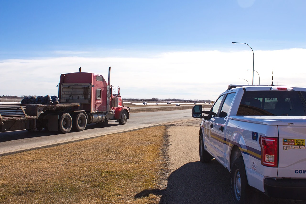 A transport truck stopped at a roadside safety inspection on an Ottawa road in autumn, with an inspector checking the vehicle and a police cruiser parked nearby.