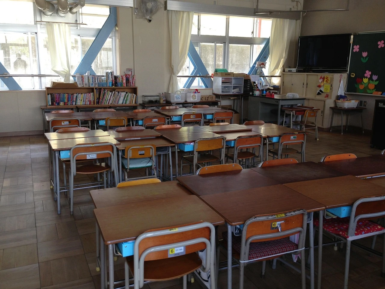 An empty elementary school classroom with rows of desks and chairs in natural window light.