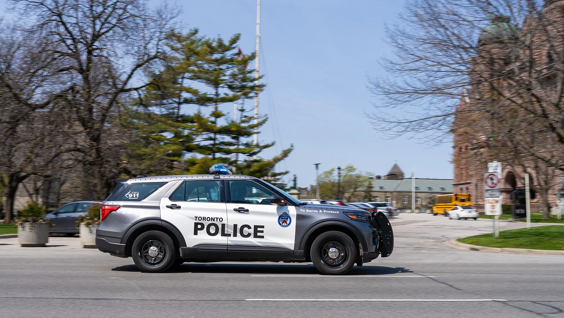 A close-up view of the exterior of a Toronto Police Service station with police cruisers parked nearby.