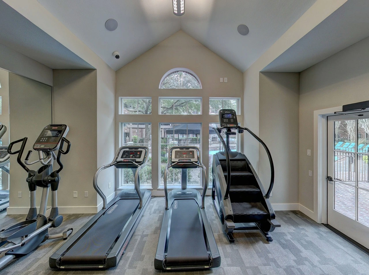 Rows of cardio machines inside a bright suburban gym, with snow visible outside the windows.